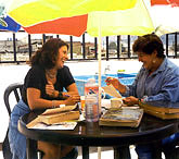 Student and teacher studying outside on a sunny day under a colorful umbrella.